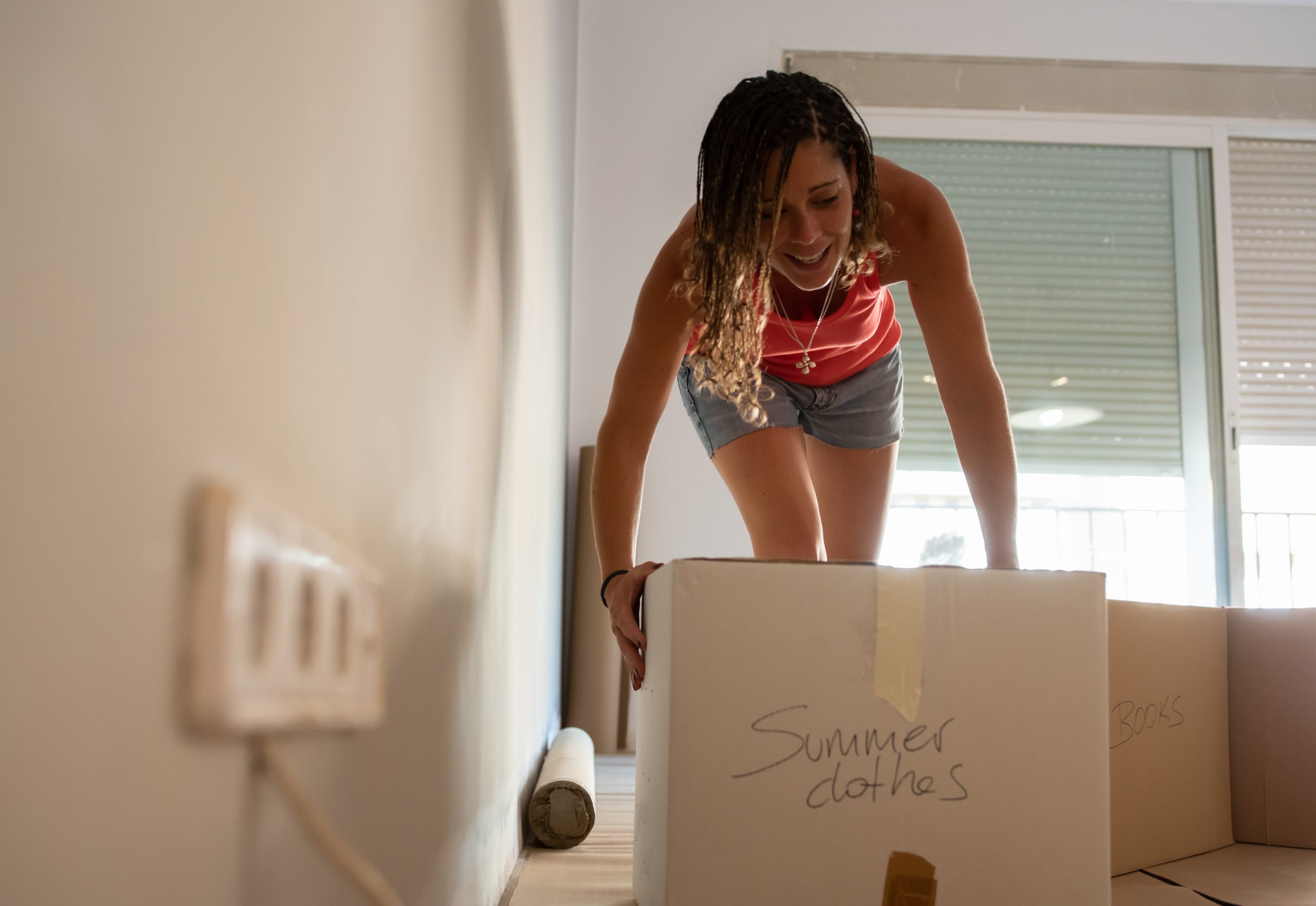 Chica en una habitación moviendo cajas, con ropa de verano.