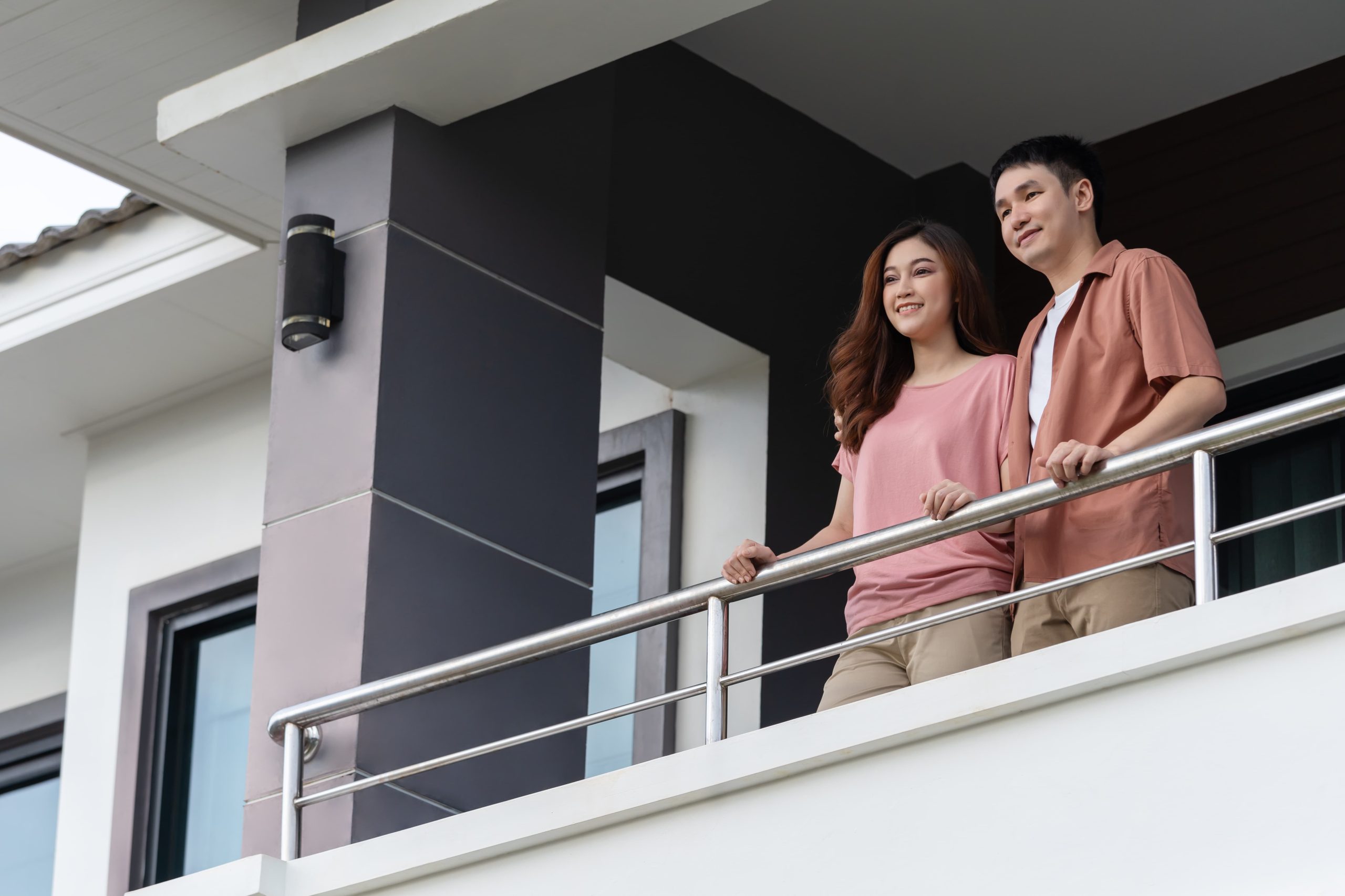 Una pareja sonriente, mirando por el balcón de su nuevo piso