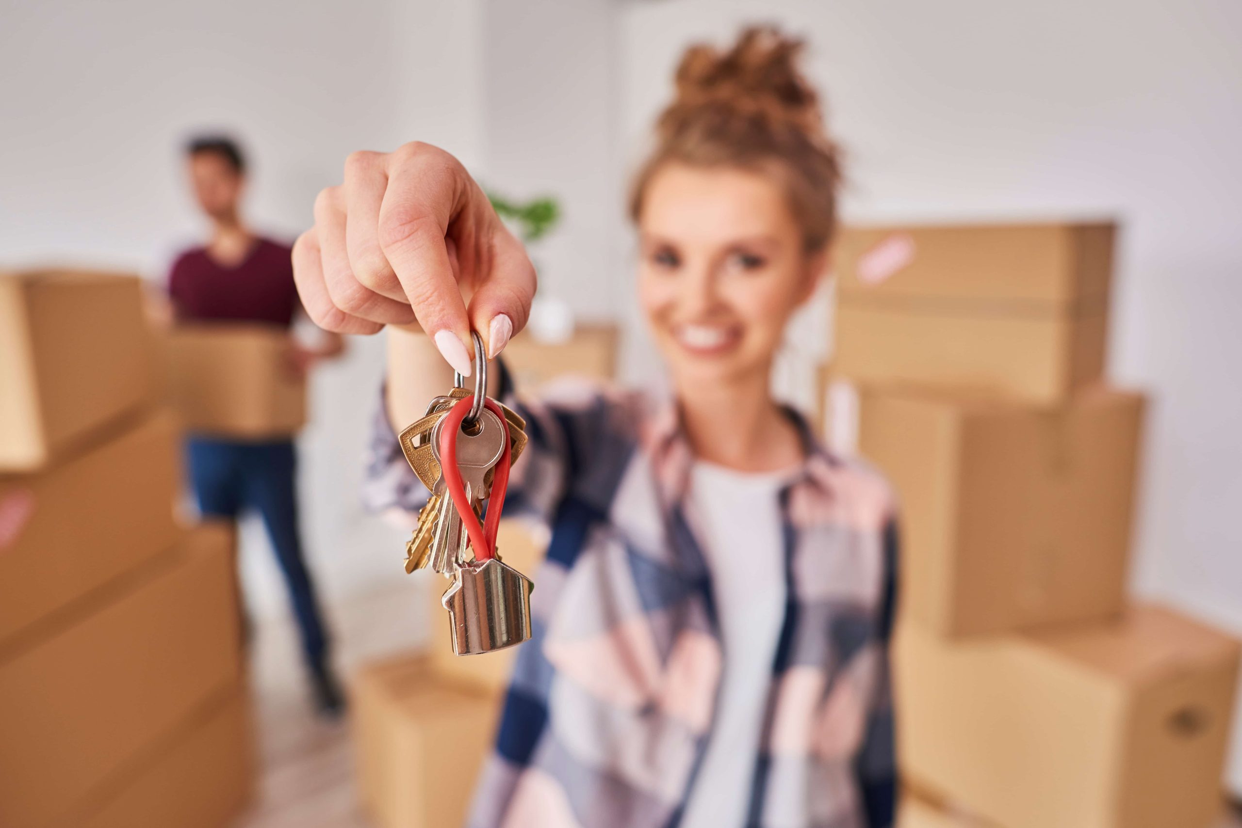 Imagen de una habitación llena de cajas de mudanza. Una chica sonriente muestra las llaves de la casa.